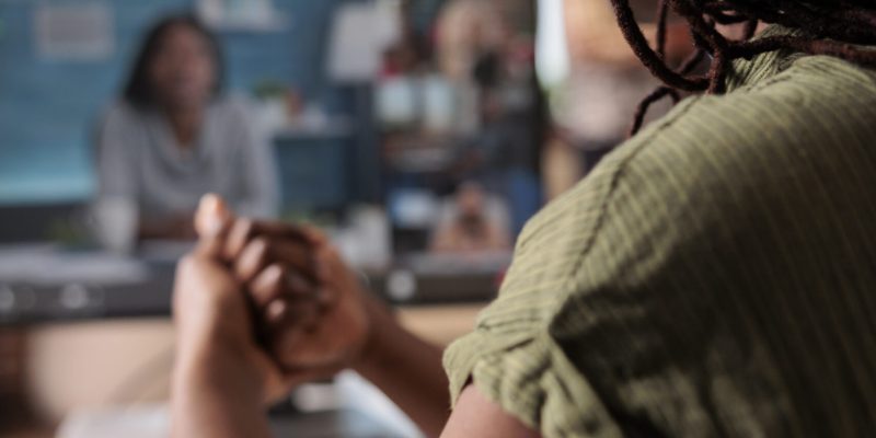 Closeup on wireless headphones on african american woman in video call with startup owner and team members. Selective focus on headset on job seeker in online interview using pc at home.